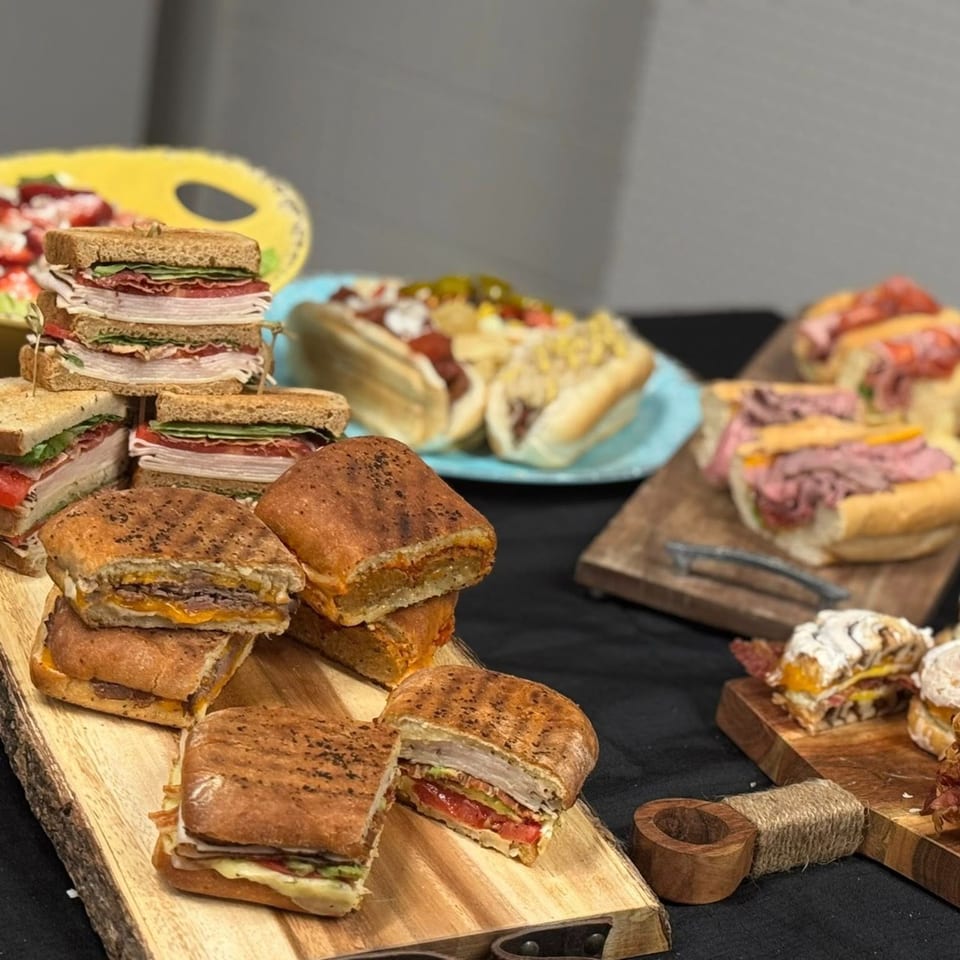 A variety of sandwiches, including paninis, subs, and club sandwiches, arranged on wooden boards.