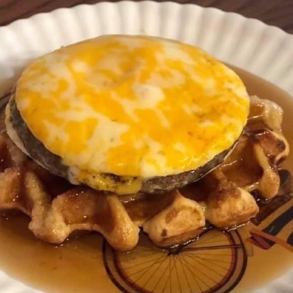Molli's Cafe breakfast sandwich with melted cheese on a sausage patty, served on a waffle with syrup.