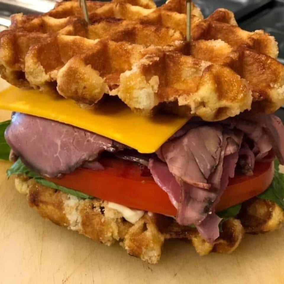 A Molli's Cafe waffle sandwich with roast beef, cheese, tomato, and lettuce, held by toothpicks.