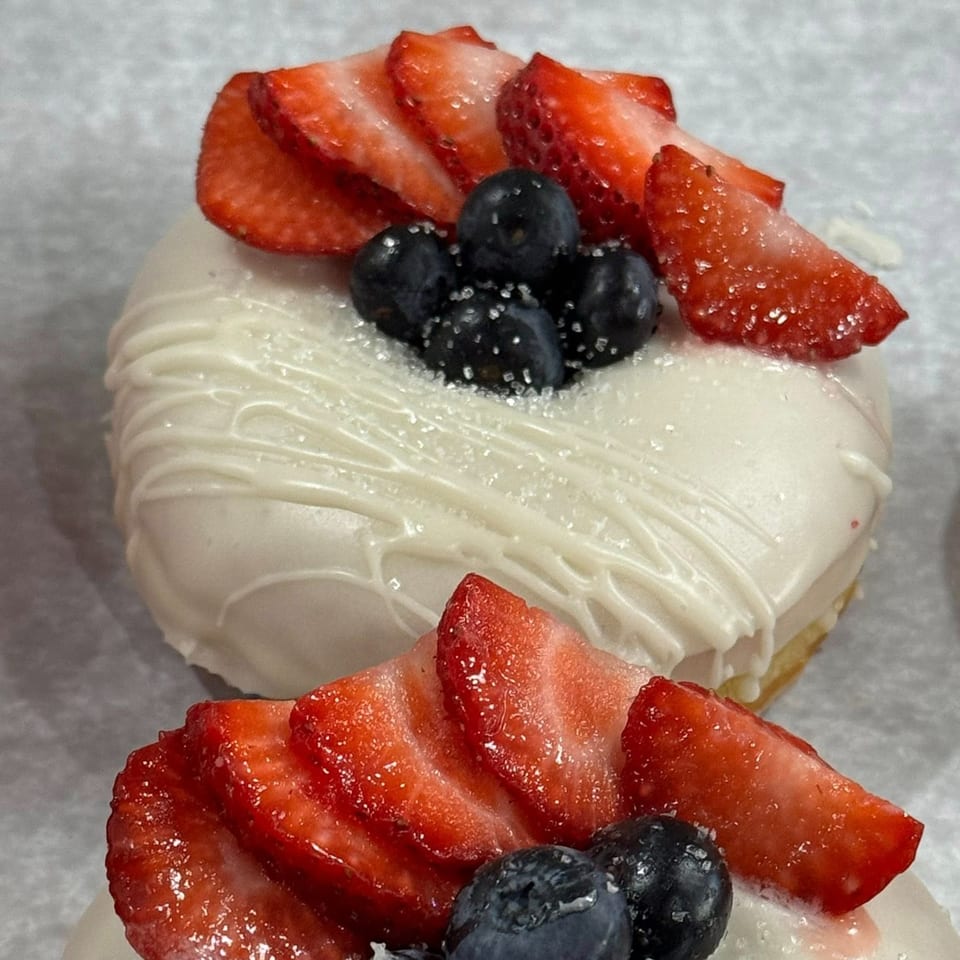 Close-up of a Molli's Cafe donut with white icing, sliced strawberries, and blueberries.